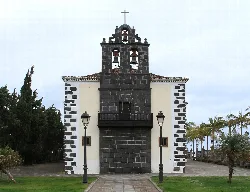 Facade of San Juan Bautista church with bell tower and trees on sides.