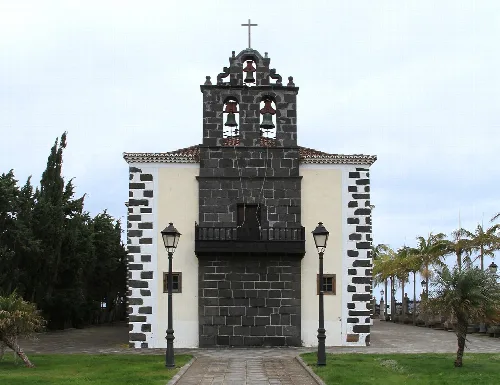 Fassade der Kirche San Juan Bautista mit Glockenturm und Bäumen an den Seiten.