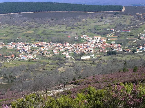 Blick auf ein Dorf mit weißen Häusern in einem Tal, umgeben von Hügeln und Vegetation.