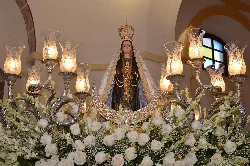 Statue der Virgen de las Nieves auf einem Thron mit Blumen und goldenen Kerzenleuchtern in einer Kirche.