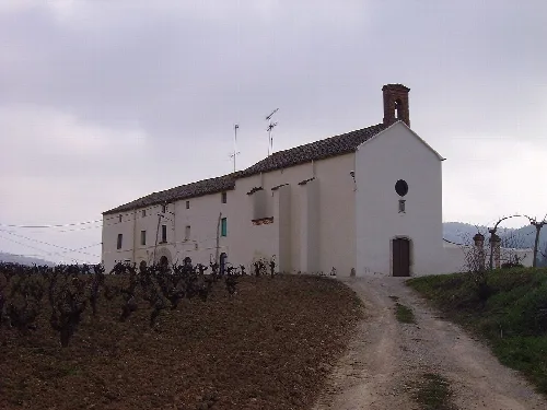 Weiße Kirche auf einem ländlichen Weg mit Weinbergen und Bergen im Hintergrund.