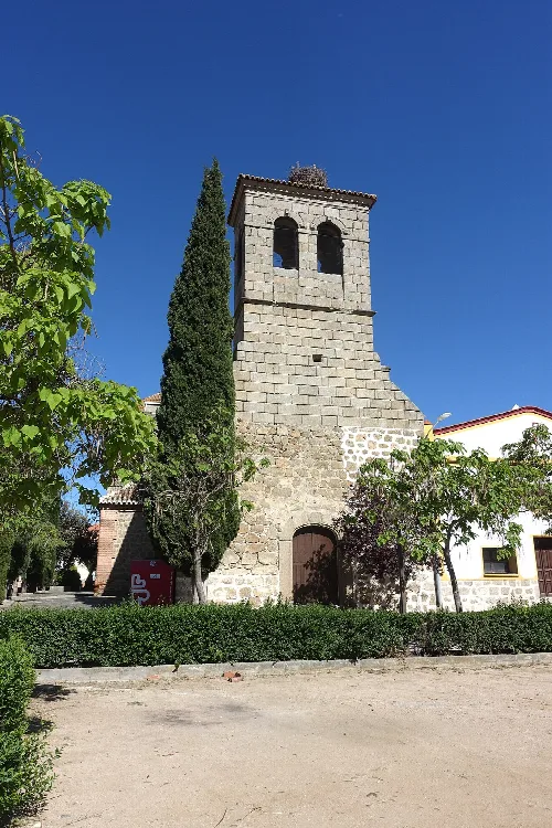 Steinerner Kirchturm mit Glockenturm und grünen Bäumen im Vordergrund.