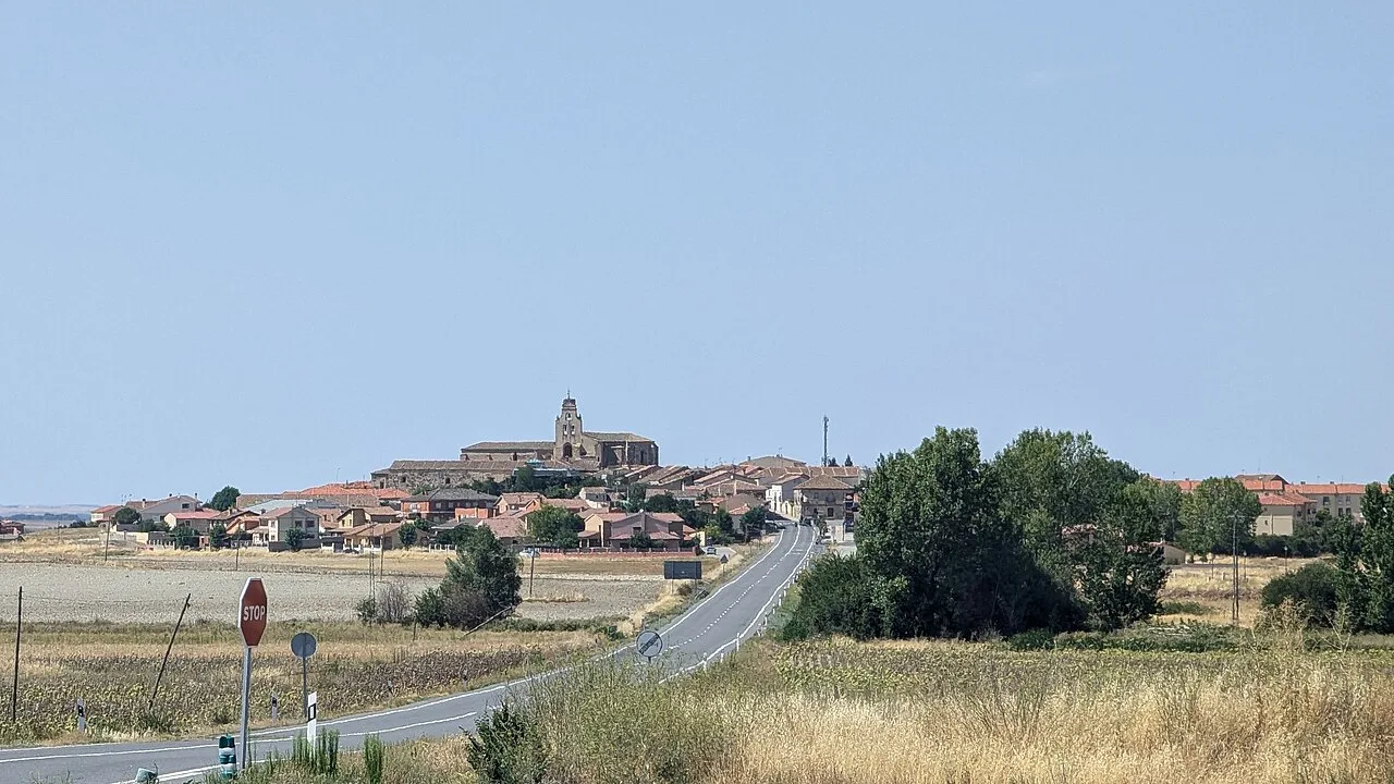 Vista de un pueblo con una iglesia en la cima de una colina y campos alrededor.