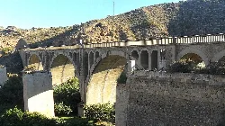 Stone bridge with multiple arches and mountain landscape.