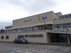 Edificio del hospital con banderas y coches aparcados.