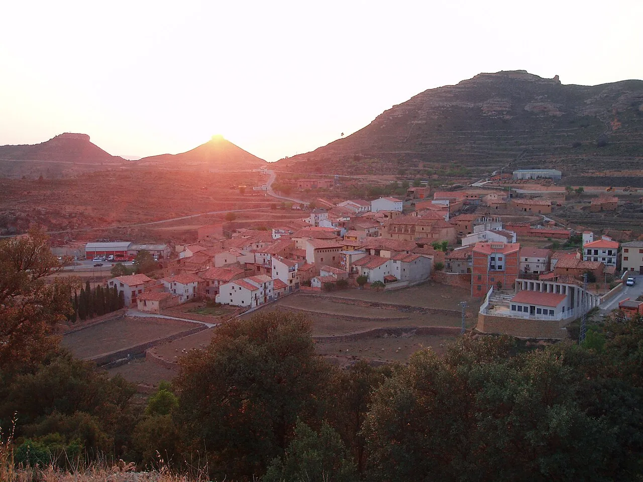 Panoramic view of a town with houses and mountains at sunset.