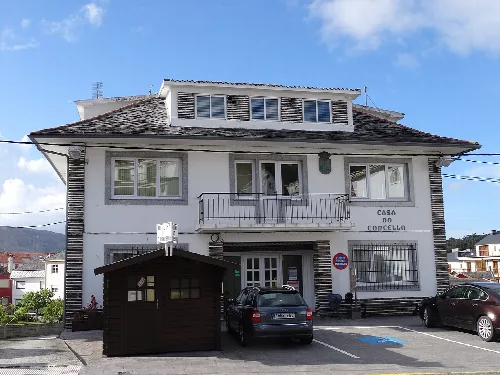 Weißes Gebäude mit einem Schild 'Casa do Concello' und Autos auf der Straße.