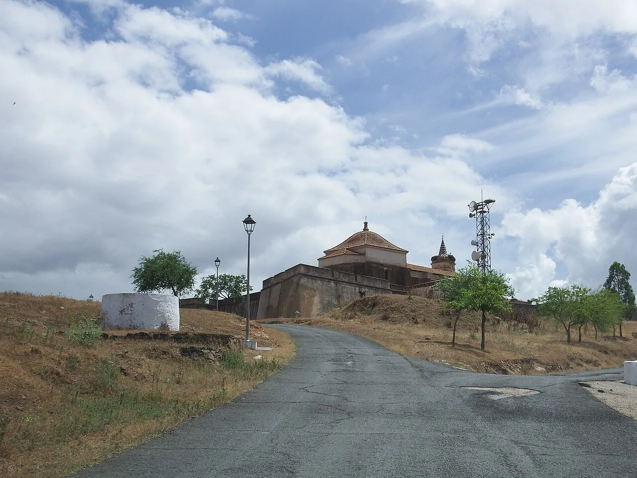 Camino asfaltado con una iglesia en la cima y árboles a los lados en Paymogo.