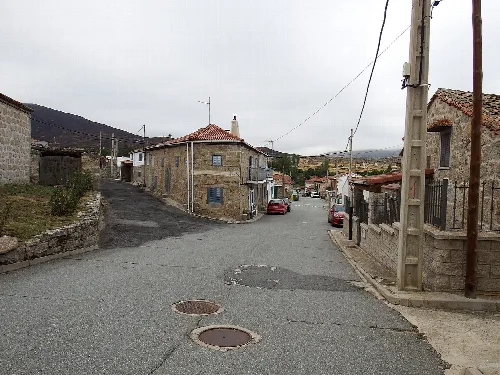 Straße in La Hija de Dios mit Steinhäusern und bewölktem Himmel.