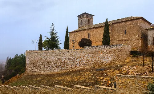 Church of St Michael the Archangel in Fuentelviejo with stone walls and cypresses.