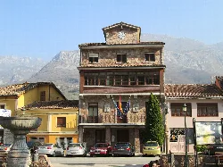 Proaza Town Hall building with flags and mountains in the background.
