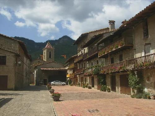 Straße mit traditionellen Häusern und Bergen im Hintergrund in Hostalets d'en Bas.