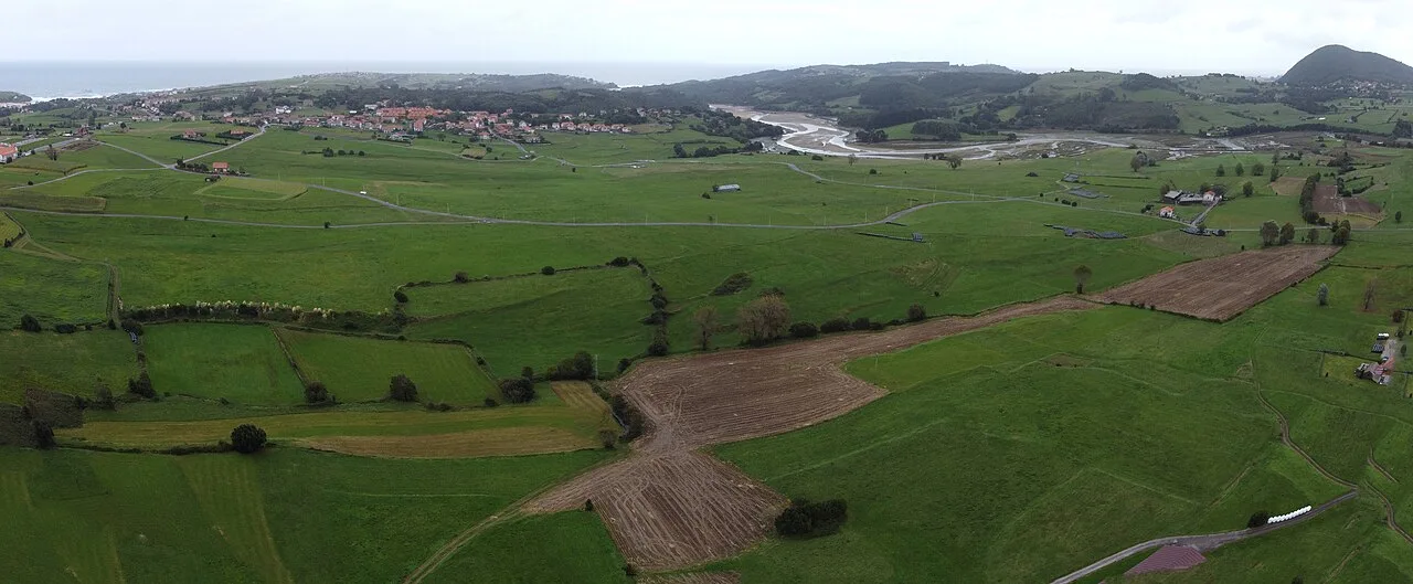 Paisaje rural con campos verdes, caminos y la ría de Ajo en el fondo.