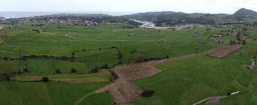 Paisaje rural con campos verdes, caminos y la ría de Ajo en el fondo.