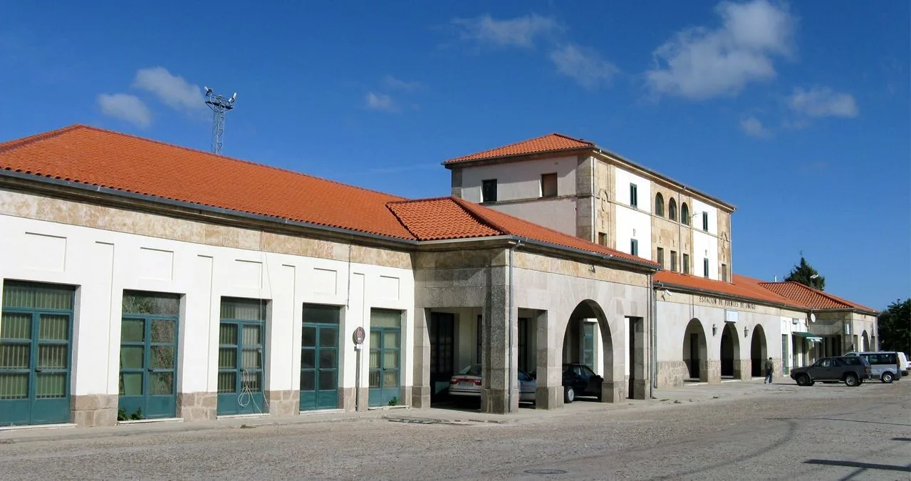 Estación de Fuentes de Oñoro con arcos, tejado de tejas rojas y coches estacionados.