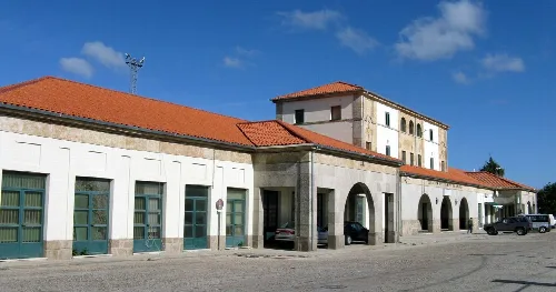Bahnhof Fuentes de Oñoro mit Bögen, rotem Ziegeldach und parkenden Autos.