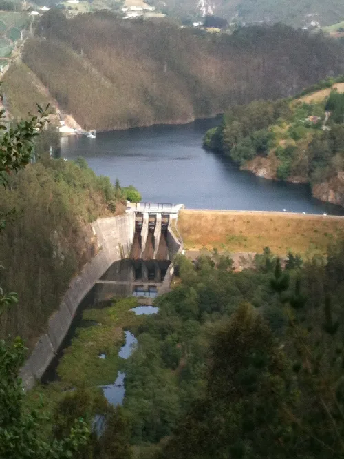 Embalse de Arbón con presa y agua rodeado de vegetación y montañas.