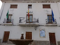 Weißes Gebäude mit Balkon und Flaggen von Spanien, der Europäischen Union und einer lokalen Flagge.