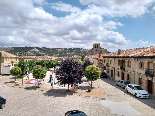 Main square with trees, benches, and church in Villahán, Palencia