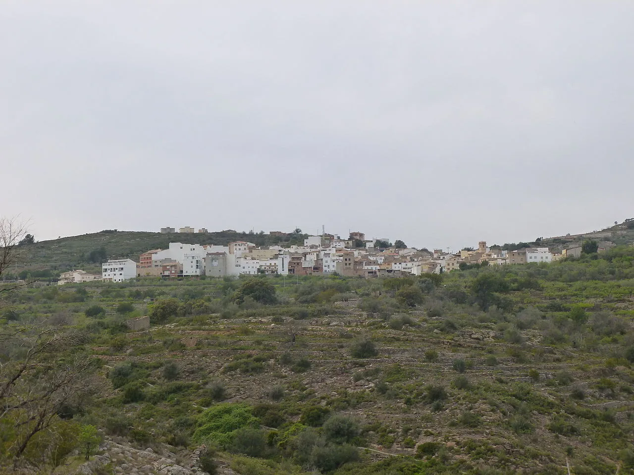 Vista panorámica de Costur con casas blancas en la colina.