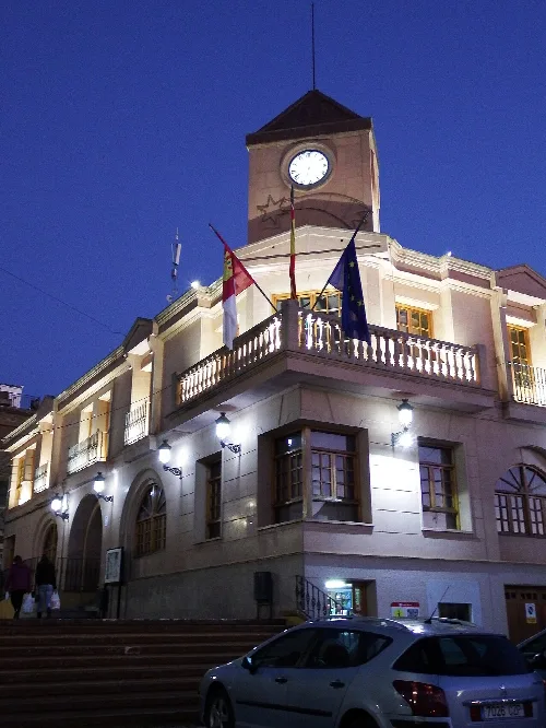 Edificio del ayuntamiento de Fuente-Álamo con banderas y reloj en la torre.