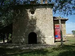 Fachada de una pequeña iglesia de piedra con puerta arqueada y ventana circular.