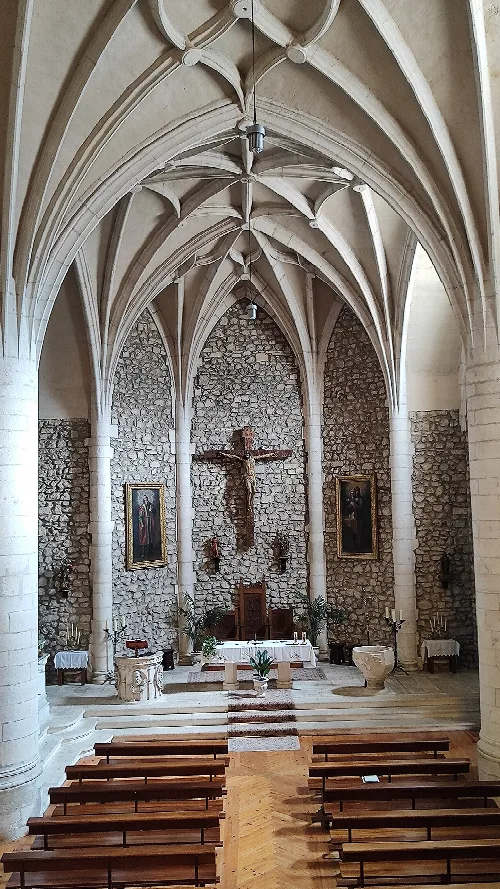Innenraum einer Kirche mit gotischen Bögen, Altar und Kreuz an einer Steilmauer.