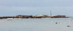 Faro y fortaleza en la costa de Cádiz con cielo nublado.