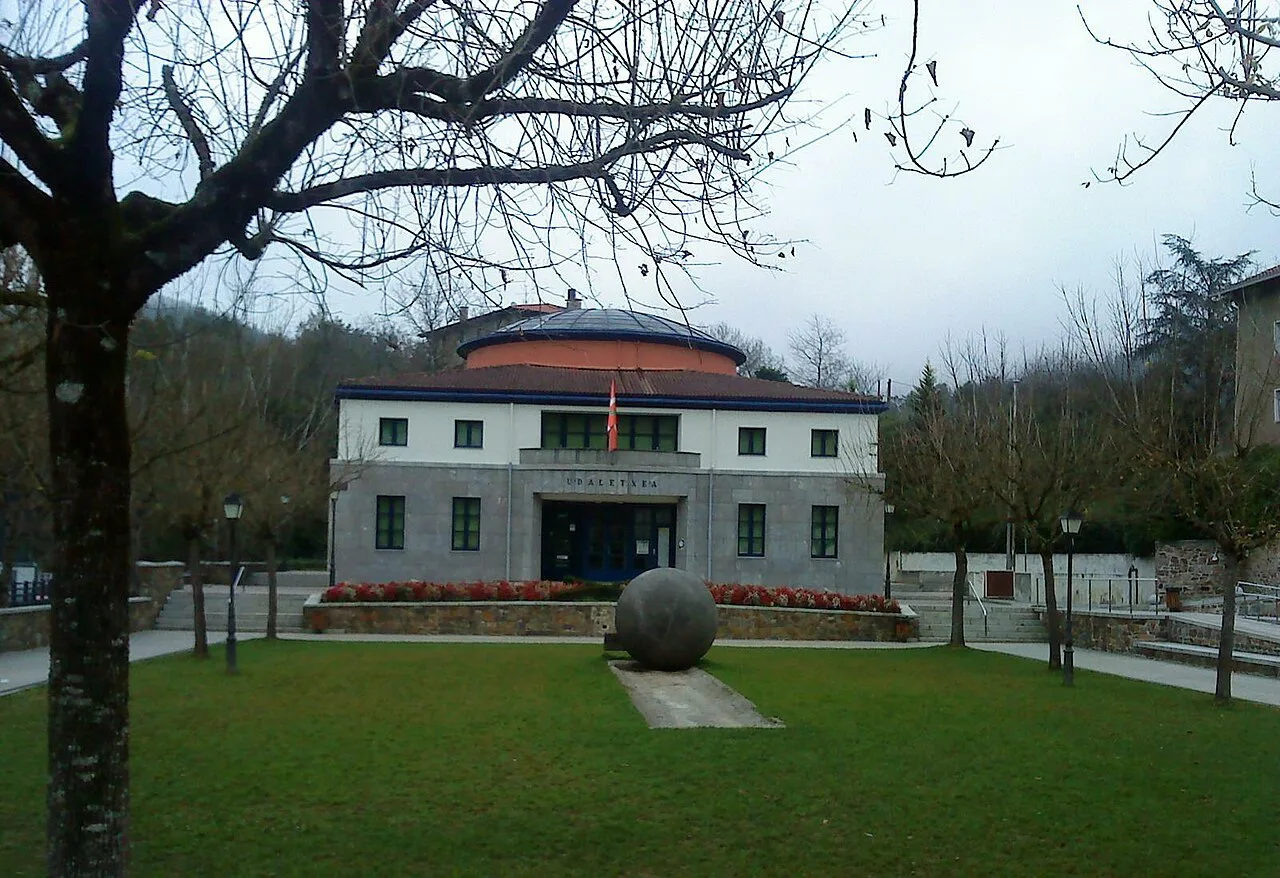 Edificio de la casa consistorial en Etxebarria, Vizcaya, con jardín y árbol en primer plano.