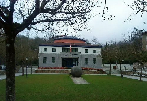 Edificio de la casa consistorial en Etxebarria, Vizcaya, con jardín y árbol en primer plano.