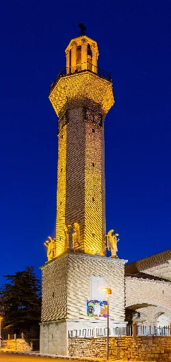Church tower with angel statues and cross at the top, illuminated against the night sky.