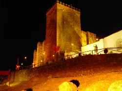 Castillo de piedra iluminado en la noche con torre y muros altos.