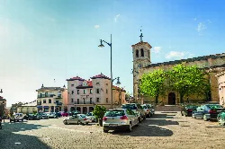Square with buildings, cars, and a church tower in Cantalejo.