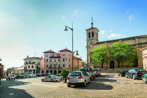 Square with buildings, cars, and a church tower in Cantalejo.