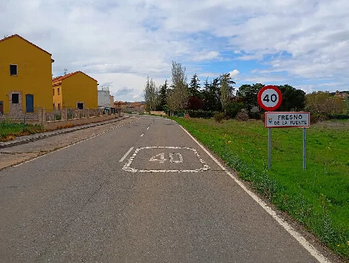 Rural road with speed limit sign and houses on the left.