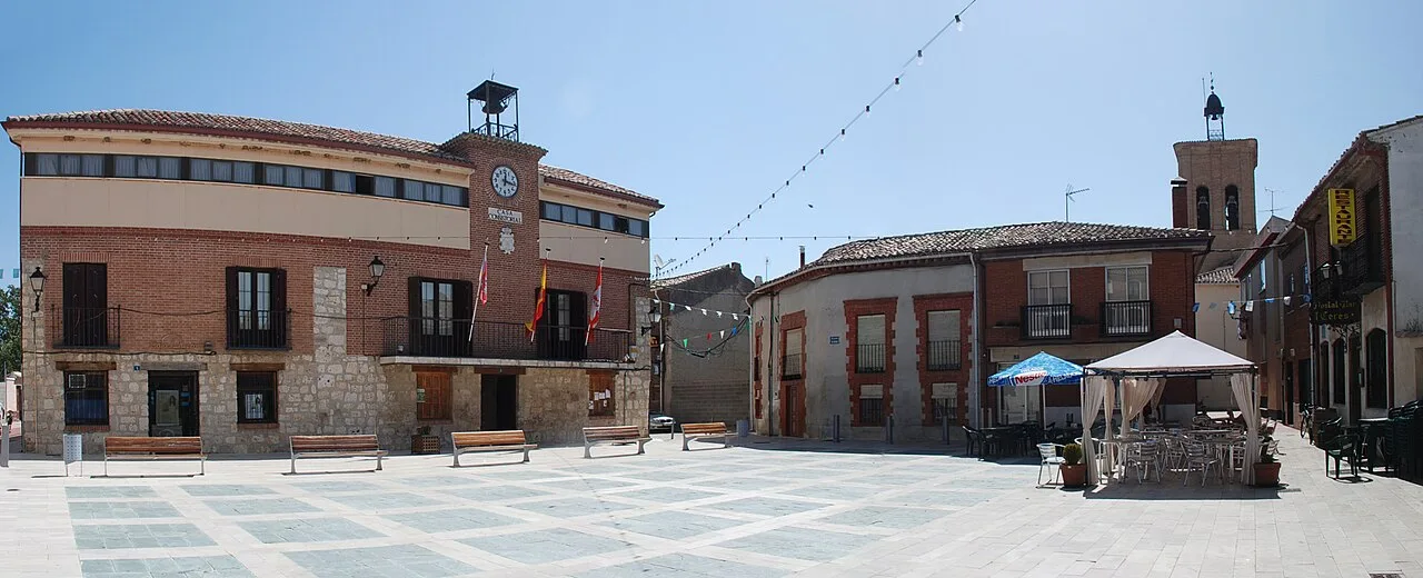 Platz in Magaz de Pisuerga mit Gebäuden und Terrasse mit Tischen und Sonnenschirmen.