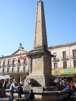 Fountain with obelisk in the square, historic buildings and carousel in Tafalla.