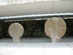 Two stone stelae in a covered space with concrete roof.