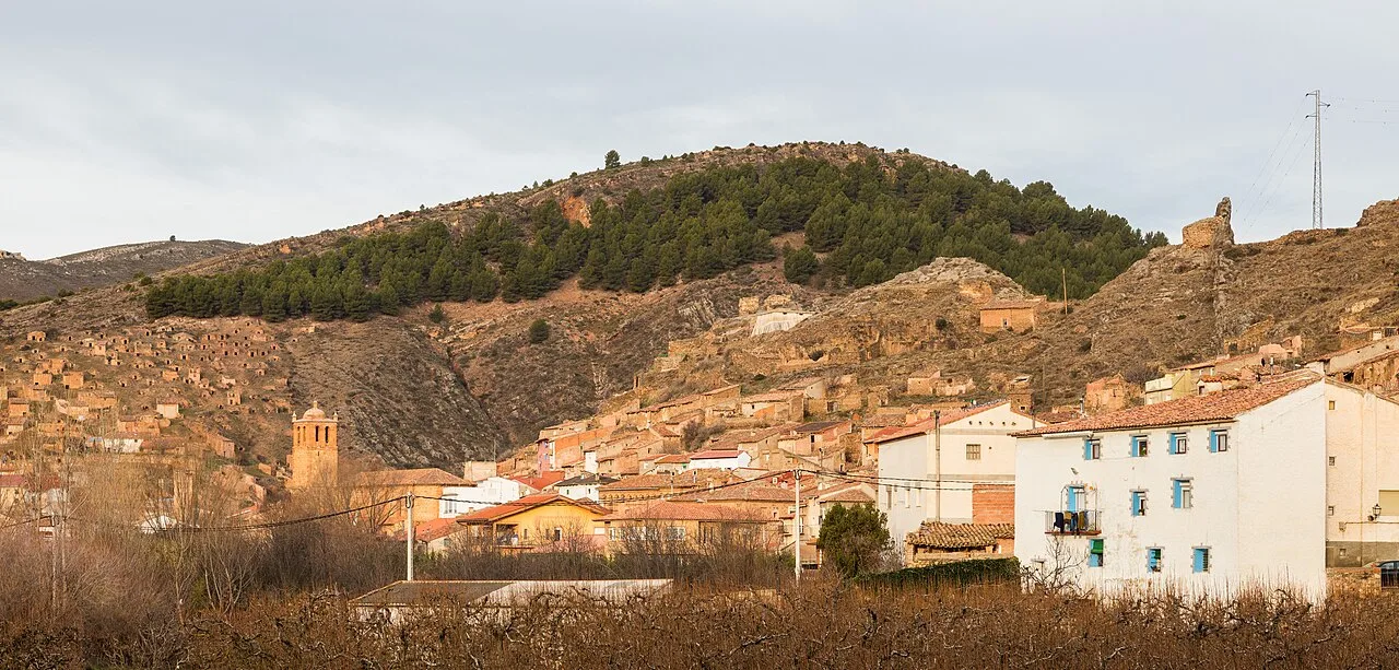White houses and rooftops in Torrijo de la Cañada with green hills behind.