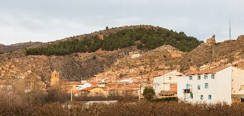 White houses and rooftops in Torrijo de la Cañada with green hills behind.