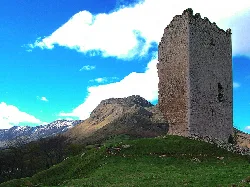 Stone tower in a mountainous landscape with blue sky and clouds.