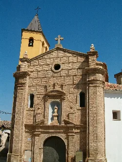 Fachada de una iglesia de ladrillo con torre y cruz en la parte superior.