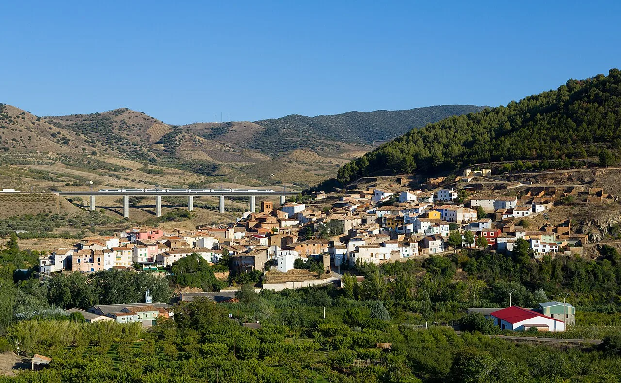 High-speed train passing through a hillside village with mountains in the background.