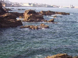 Felsen im Wasser im Hafen von Burela mit der Stadt im Hintergrund.