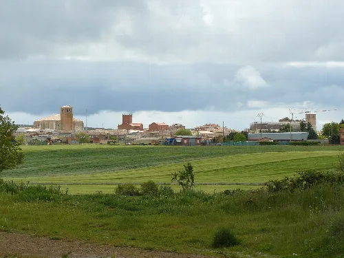 Landscape with green fields and town in the distance under cloudy sky.