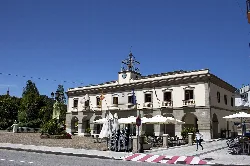Gebäude mit Uhr und Terrasse in Vegadeo, Asturien, mit Tischen und Sonnenschirmen auf dem Platz.
