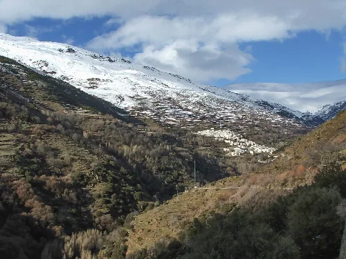 Berglandschaft mit weißen Häusern in Trevélez und Schnee auf den Gipfeln.
