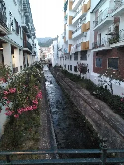 Fluss im Zentrum von Ubrique mit Gebäuden auf beiden Seiten und Pflanzen entlang des Flusses.