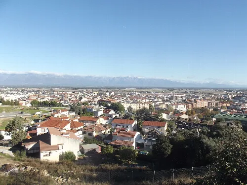 Stadtansicht mit Häusern und schneebedeckten Bergen im Hintergrund.