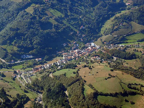 Vista aérea de un pueblo rodeado de montañas y bosques en Asturias.